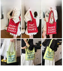 Detail view of canvas tote bags in red and light green with repeated HAPPY text print
