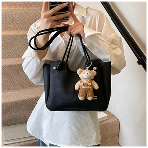 Detail of black lychee grain leather tote bag featuring a cute plush bear pendant