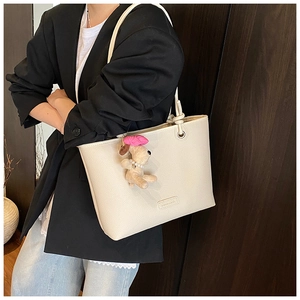 Close-up of beige tote bag with litchi grain texture and a cute plush puppy pendant