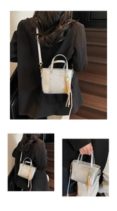 Detailed view of silver textured bucket bag with gold hardware and woven tassel detail