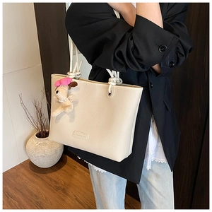 Detail of cream tote bag featuring lychee grain leather and knotted rope handles with charm