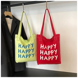 Detail of green and red canvas tote bags with HAPPY lettering hanging on a rack