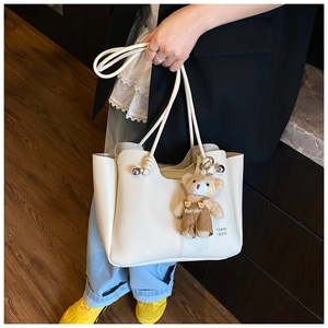 Detail of white lychee pattern tote bag featuring a knotted handle and cute bear charm