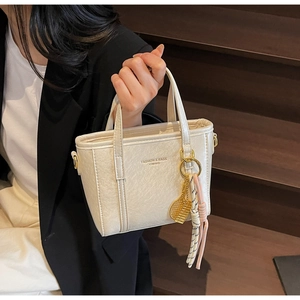 Detail of cream leather bucket bag with gold hardware and woven tassel charms