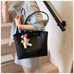 Detail of black pebbled leather tote bag featuring a cute plush dog charm with pink bow
