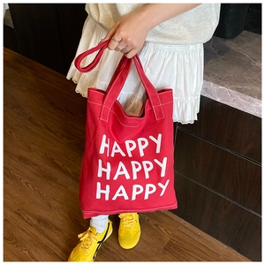 Detail of red canvas tote bag with Happy typography, showing dual handles and shoulder strap