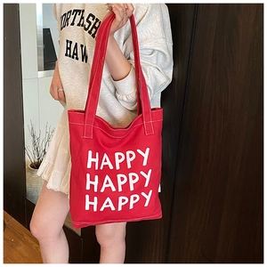 Detail of red canvas tote bag with Happy lettering print being worn by a model