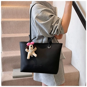 Detail of black pebbled leather tote bag with a cute plush dog charm on a strap