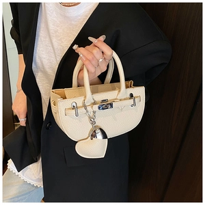 Detail of beige litchi grain leather bag with silver lock and heart charm