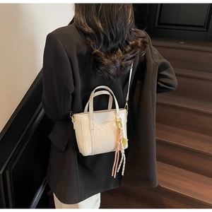 Fashion bucket bag in cream white PU leather with gold hardware and tassel detail worn by model