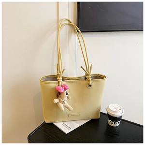 Detail of cream yellow lychee texture tote bag with a cute puppy plush charm on a table