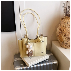 Detail of light yellow lychee pattern tote bag with teddy bear charm on luggage