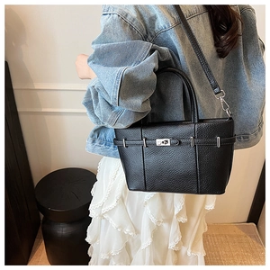 Détail du sac seau noir en cuir grainé avec fermoir rotatif argenté sur un jean