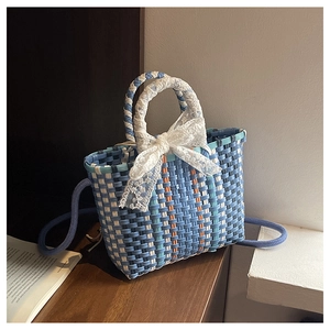 Détail d'un sac panier tissé coloré avec un nœud en dentelle blanche et bandoulière bleue