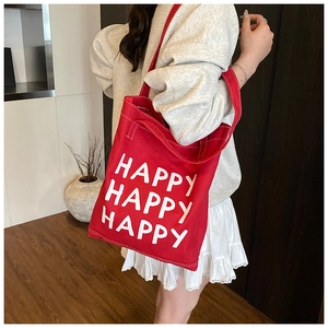 Detail of red canvas tote bag with Happy lettering and dual shoulder straps shown on model