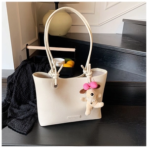 Detail of beige pebble leather tote bag with knotted strap and cute puppy pendant