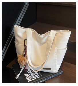 Detail of white minimalist tote bag with cute brown plush bear pendant on wooden stairs