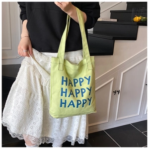 Detail of lime green canvas tote bag with Happy prints worn by a model in casual style