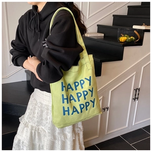 Detail view of large green canvas tote bag featuring blue triple Happy letter printing