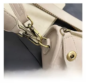 Gros plan des crochets en métal bronze et coutures fines sur le sac d'épaule en cuir beige