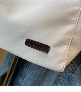 Detailed close-up of SHANHEYC leather logo patch on white canvas tote bag