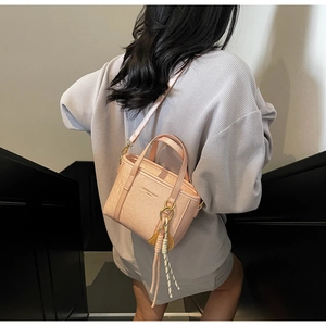 Pink bucket bag with lychee texture and braided charm shown in a lifestyle street setting