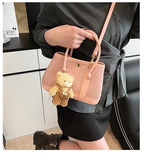 Detail of pink woven bucket bag featuring a cute plush bear charm and crossbody strap