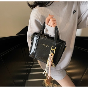Detail of black bucket bag featuring glossy leather texture and gold hardware accents