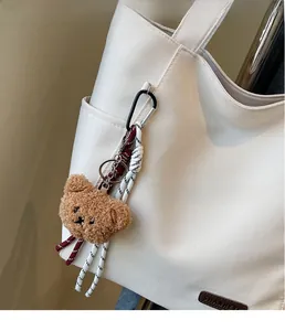 Close-up of a brown plush bear keychain with woven ropes on a white canvas tote bag