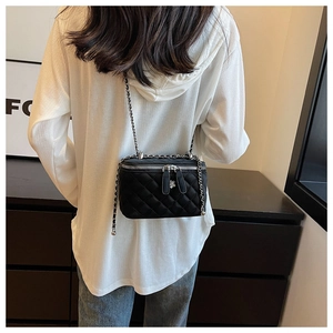 Detail of a black quilted shoulder bag with camellia charm and woven chain strap