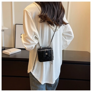 Detail of black quilted crossbody bag with silver flower charm and metal chain strap