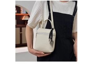 Détail d'un sac carré blanc crème en cuir grainé avec un pendentif cœur argenté et nœud