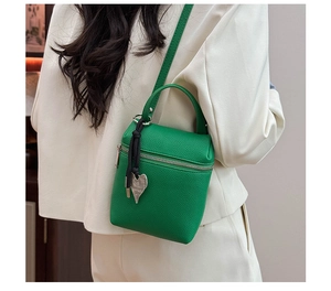 Détail du mini sac carré vert en cuir grainé avec pendentif coeur sur un tailleur blanc