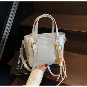 Detail of silver bucket bag with metallic texture, gold buckle and woven pendant charm
