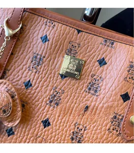 Close-up of brown textured leather bag featuring gold logo plate and bear pattern print