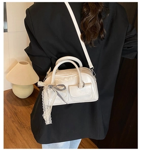 Détail du sac Boston en cuir verni blanc cassé avec nœud en dentelle et deux poches