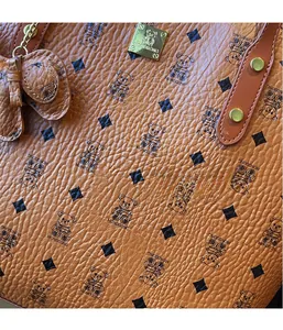 Detail of brown lychee leather bag featuring teddy bear print and golden logo plate