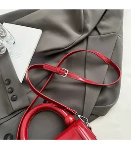Détail d'un sac à main rouge en cuir ciré avec bandoulière réglable et boucle argentée
