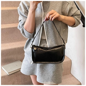 Détail du sac baguette noir brillant avec boucle dorée et texture en cuir lisse