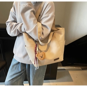 Detail of canvas tote bag featuring plush bear pendant and stylish braided rope decoration