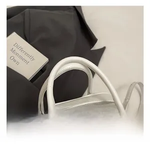 Close-up of white leather handbag with metal zipper and bow accent on the handle