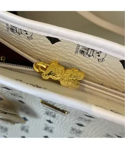 Detail of the golden bear-shaped metal zipper pull on a white printed leather handbag