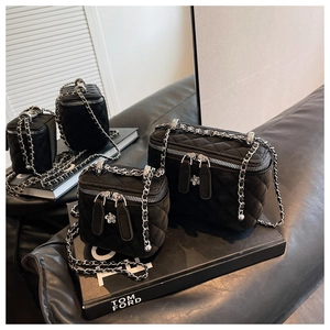Detail of black quilted vanity bags with camellia zipper pulls and leather chain strap