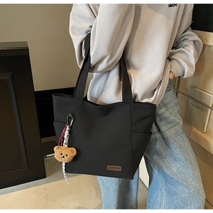 Detail of black canvas tote bag with brown leather logo and cute plush bear charm