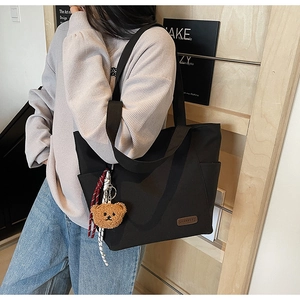 Detail of black canvas tote bag with brown leather label and plush bear keychain ornament