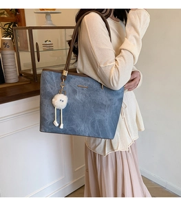 Detail of blue-gray tote bag with leather straps and cute plush pendant in a cafe