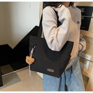 Detail view of the black canvas tote bag showing side pockets and a cute bear charm
