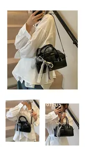 Detail of black glossy leather Boston bag featuring lace bow and dual front pockets