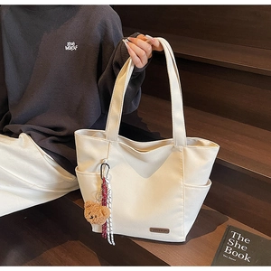 Close-up of a cream canvas tote bag with side pocket and brown plush bear charm detail