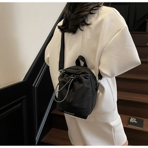 Rear view of a model wearing the OOMTAO black nylon drawstring mini backpack in a city setting
